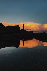 Silhouette of woman on lake against sky during sunset