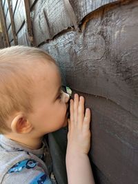 Close-up of boy looking through hole in wooden wall