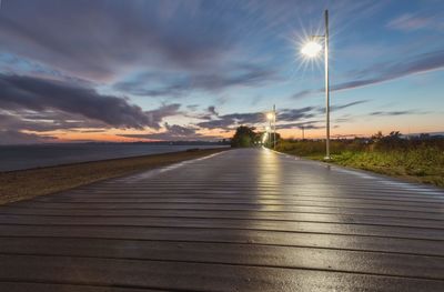 Road by sea against sky during sunset