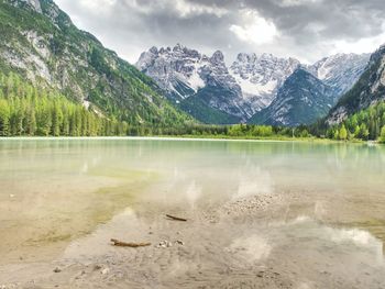 Blue green lake between sharp rocky mountains. smooth water surface, the alps peaks against clouds