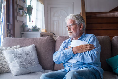 Senior man holding paper while sitting on sofa at home