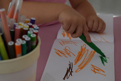 Close-up of boy holding multi colored pencils on table
