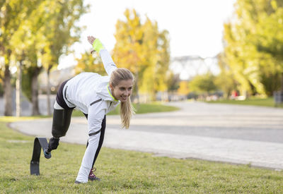 Side view of professional female runner with leg prosthesis preparing for explosive start during training in park
