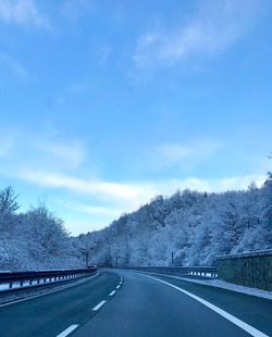 Road by trees against sky during winter