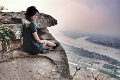 Side view of young woman sitting on rock
