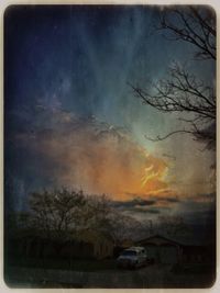 Bare trees on field against cloudy sky