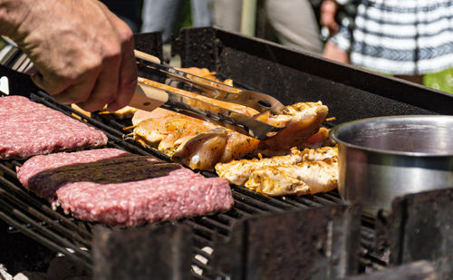 Close-up of man holding utensil and grilling meat in back yard.