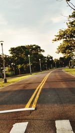 Empty road by trees against sky in city