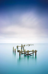 Wooden posts in sea against sky