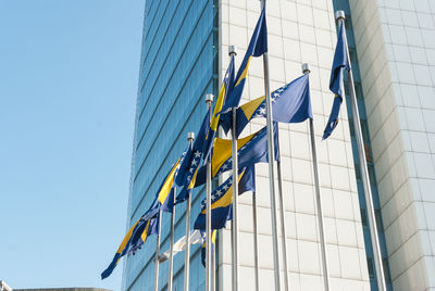 Low angle view of bosnia and herzegovinan flags and modern building against clear blue sky