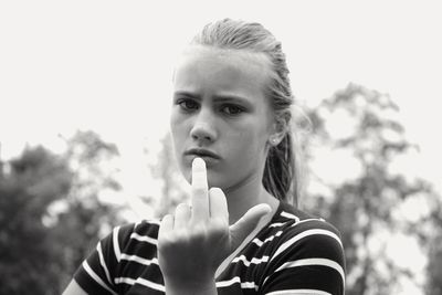 Portrait of teenage girl showing obscene gesture against sky