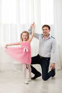 Portrait of cute girl dancing with father against curtain at home