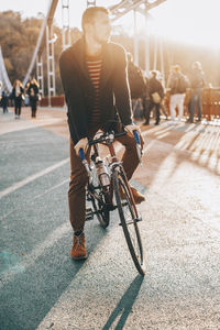 Male cyclist looking away while riding bicycle on bridge in city during sunset