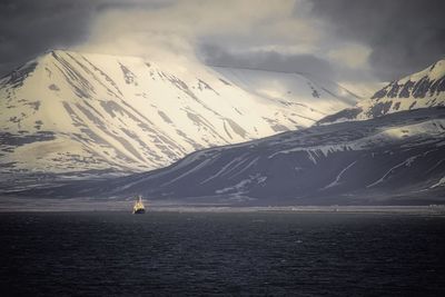 Scenic view of sea by snowcapped mountains against sky