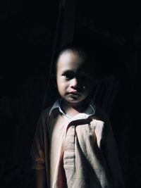 Portrait of boy standing against black background