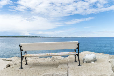 Deck chairs on shore by sea against sky