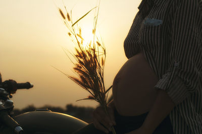 Midsection of pregnant woman against sky during sunset