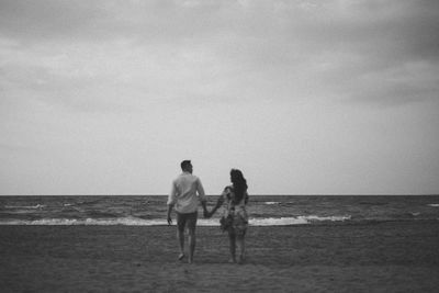 Back view of people walking at beach against sky