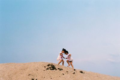 Siblings on sand at beach against clear sky