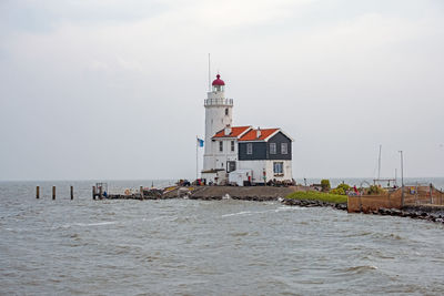 Lighthouse amidst sea and buildings against sky