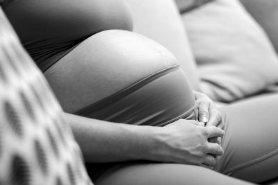 Midsection of woman sitting on bed at home