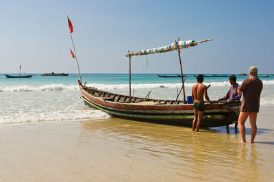 Rear view of men with boat standing at beach