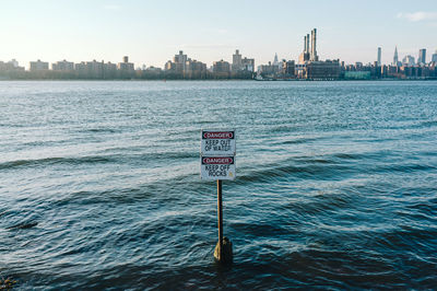 Information sign by sea against sky in city