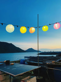 Street lights hanging by sea against clear blue sky