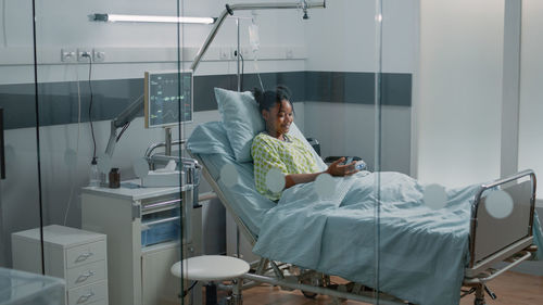 Happy woman using smart phone on bed at hospital
