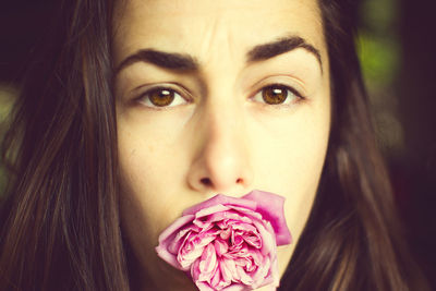 Close-up portrait of young woman with pink rose in her mouth
