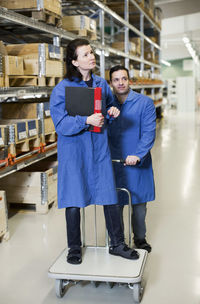 Male electrician pushing trolley while woman standing on it while working in factory