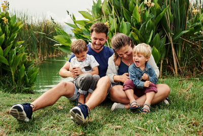 Full length of happy family sitting by pond