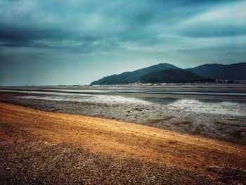 View of calm beach against cloudy sky