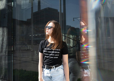 Young woman wearing sunglasses standing against buildings in city
