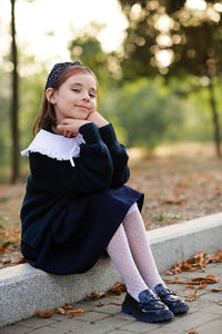 Cute smiling child pupil girl 6-7 year old wear school uniform posing in patk outdoor.