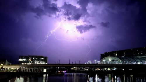 Lightning illuminated bridge against stormy sky at night