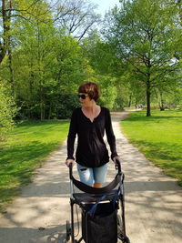 Woman with wheelchair walking on footpath against trees