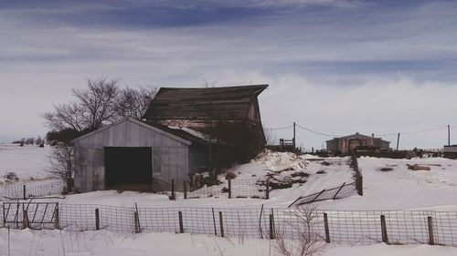 Barns on snow covered field against sky during winter