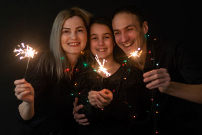 Happy family in black - woman, man and little girl, with a sparkler in hand the new year's christmas