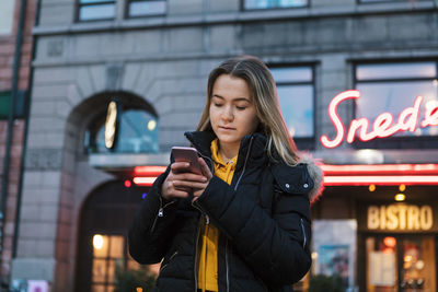 Young woman using smart phone while standing in illuminated building