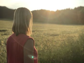 Rear view of woman standing on land against sky during sunset