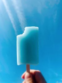 Human hand holding ice cream against blue sky