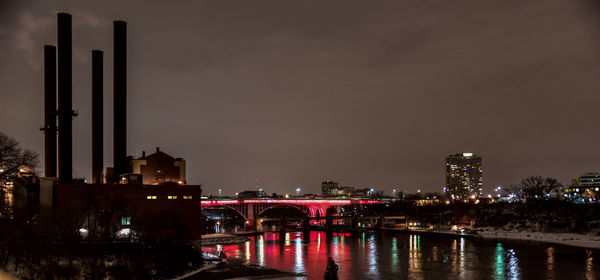 Illuminated bridge over river in city against sky