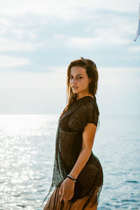 Portrait of young woman standing by sea against sky