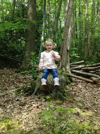 Full length portrait of cute girl sitting in forest