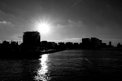 Silhouette buildings by river against sky in city