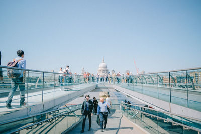 People walking on bridge against clear sky