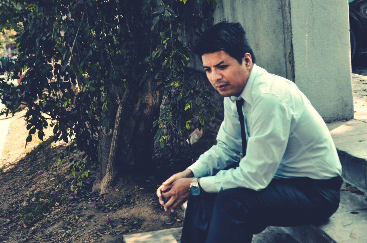 young men, one person, young adult, real people, sitting, tree, leisure activity, day, plant, three quarter length, nature, formalwear, lifestyles, men, casual clothing, males, focus on foreground, outdoors, contemplation