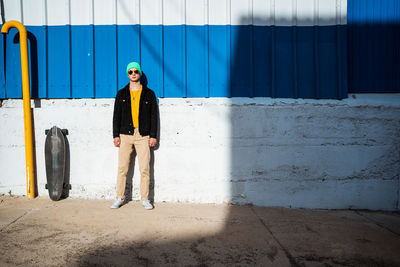 Portrait of young man wearing sunglasses standing against wall