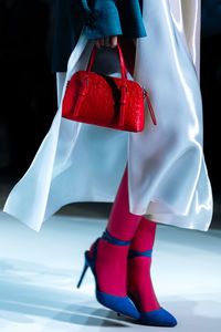 Fashionable details of a white silk dress and a red handbag in a woman's hand. elegant clothing 